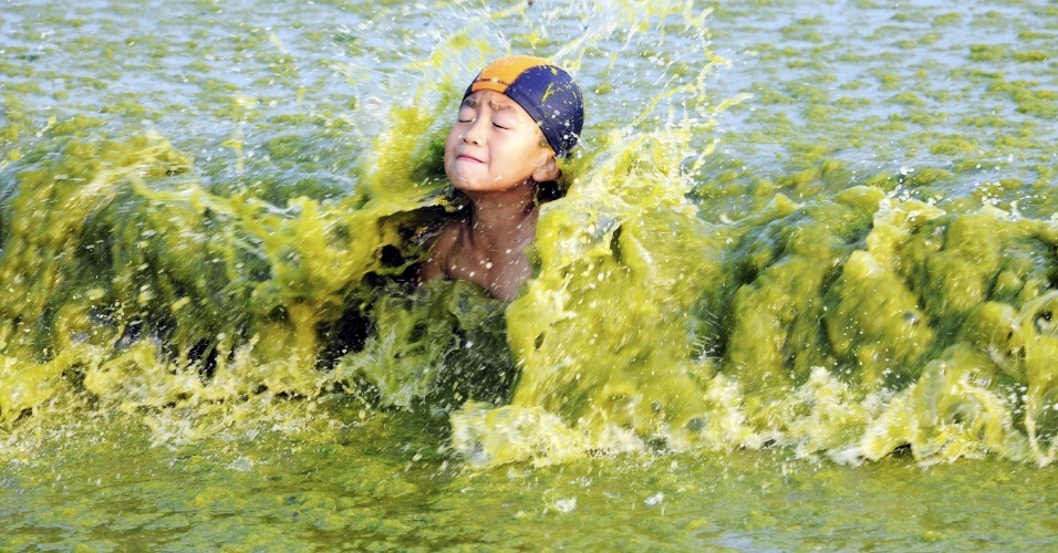 03.ago.2015 - Garoto fecha os olhos com a chegada de uma onda com água colorida por algas, em praia de Qingdao, na China