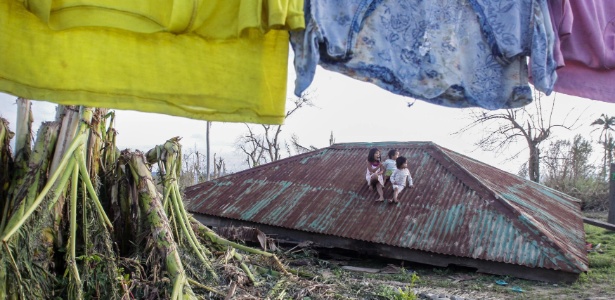 Crianças ficam sentadas no telhado de uma casa arrancado pelo tufão Koppu no vilarejo de Casiguran, no norte das Filipinas - Dante Diosina/AFP