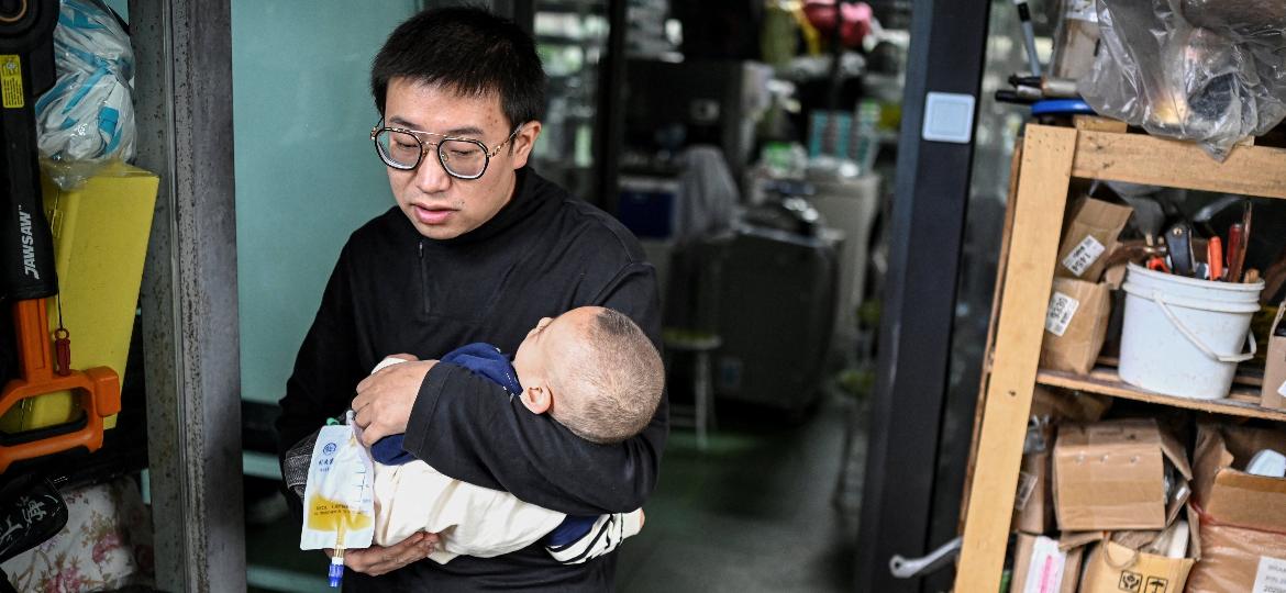 A foto tirada em 20 de outubro de 2021 mostra Xu Wei segurando seu filho Xu Haoyang, que foi diagnosticado com síndrome de Menkes, saindo de seu laboratório doméstico em Kunming, na China - Jade GAO / AFP