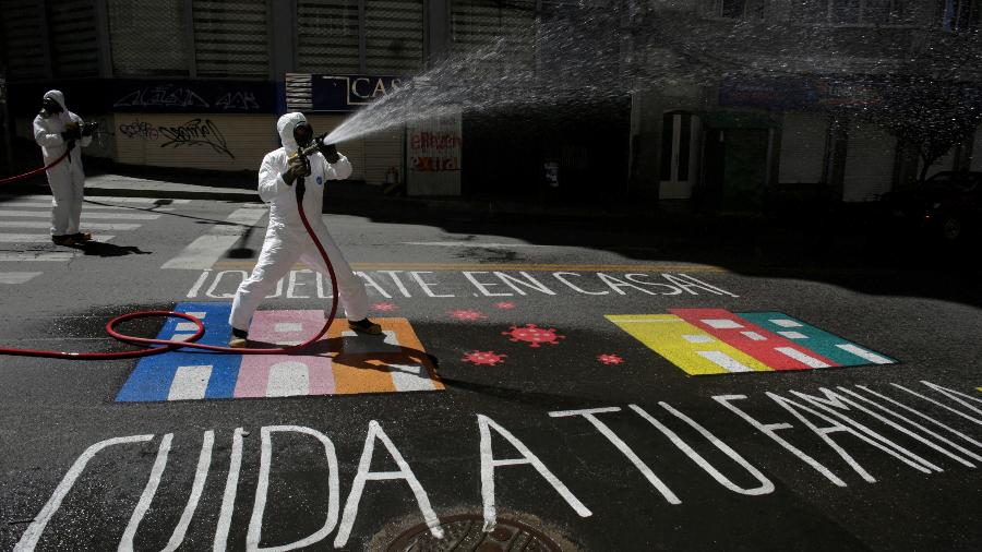 Profissionais de saúde pública usam desinfetante para limpar uma rua, enquanto um grafite no chão diz "Fique em casa, cuide da sua família", em La Paz, Bolívia - MANUEL CLAURE/REUTERS