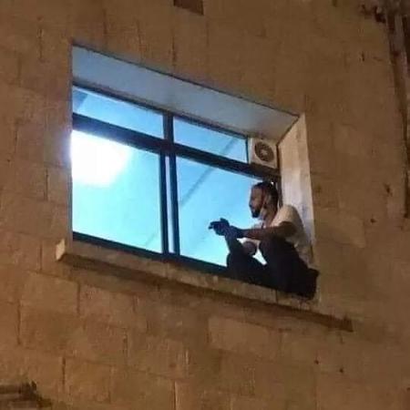 Jihad Al-Suwaiti, palestino de 30 anos, senta no parapeito da janela de um hospital na Cisjordânia onde a mãe estava internada com covid-19 - Reprodução