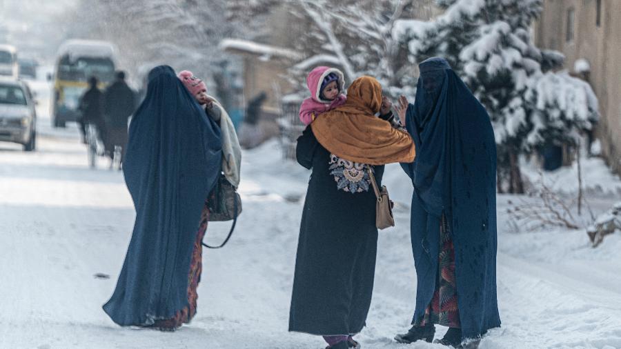 23.01.2023 - Mulheres afegãs carregam crianças enquanto caminham por uma rua coberta de neve em Cabul - Wakil Kohsar/AFP