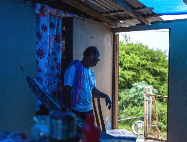 Pablo Figueroa sob a lona que cobre as partes que faltam do seu telhado, em Punta Santiago, Porto Rico - Dennis M. Rivera Pichardo/The New York Times