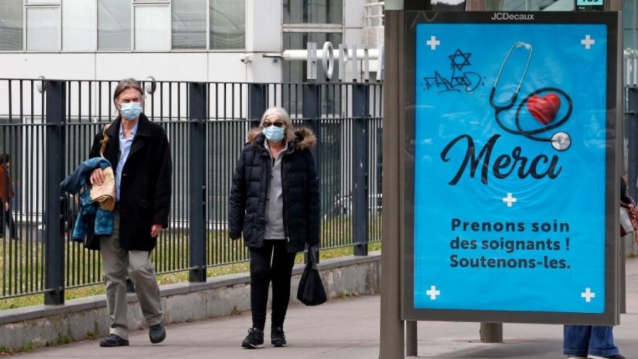 4.mai.2020 - De máscara, casal caminha por rua de Paris, na França. À direita, um anúncio diz: "Obrigado, cuide e apoie os profissionais de saúde" - Chesnot/Getty Images