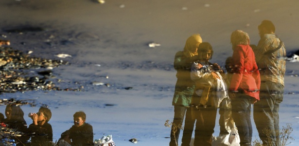 Imagem de refugiados é refletida em piscina, enquanto esperam trem na Macedônia