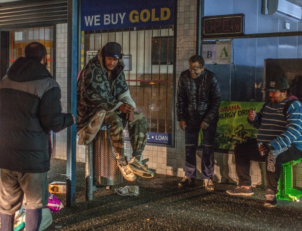 Moradores de rua sentam e conversam do lado de fora de uma loja de penhores em Henderson, na Nova Zelândia - Asanka Brendon Ratnayake/The New York Times