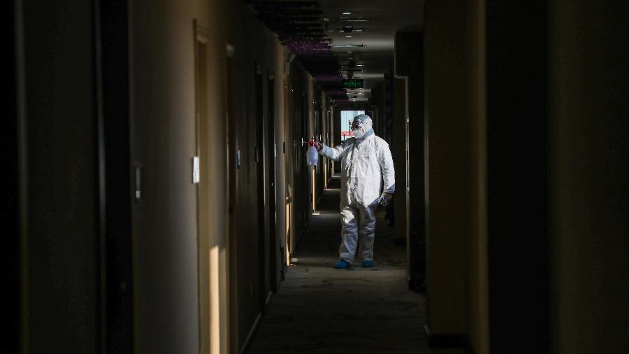 Membro da equipe médica desinfetando um hotel convertido em zona de isolamento na província de Hubei, China - STR/AFP