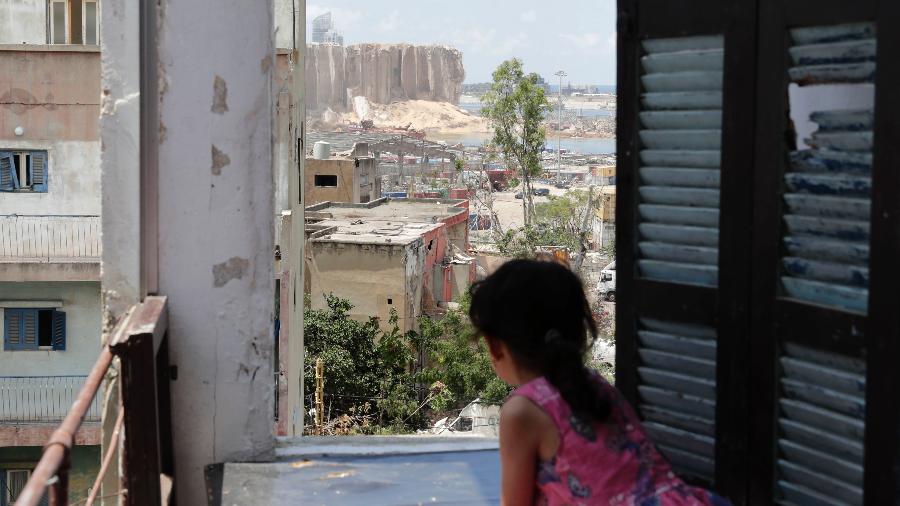 Menina olha para o Porto de Beirute destruído da janela da sua casa - ANWAR AMRO/AFP