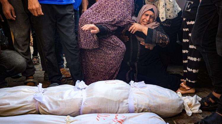 Mulheres palestinas choram ao lado dos corpos cobertos de três crianças mortas em um bombardeio israelense; elas tinham idades entre cinco e nove anos