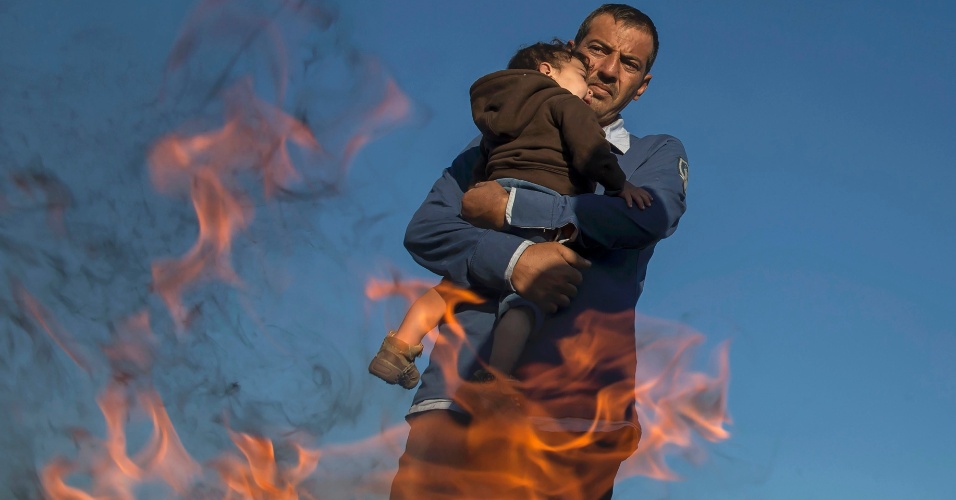 8.set.2015 - Refugiado segura criança no colo enquanto se aquece junto ao fogo em um acampamento improvisado no município de Röszke, na Hungria