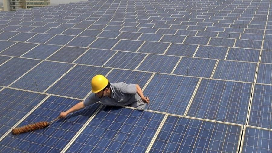 Funcionário limpa painéis de energia solar na China; país aposta em tecnologias verdes para sustentar crescimento