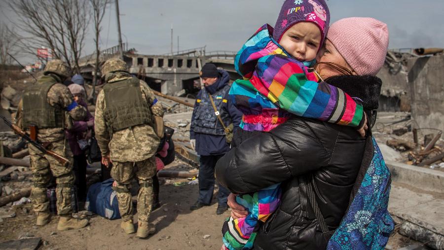 28.mar.2022 - Uma mulher segura uma criança ao lado de uma ponte destruída durante a evacuação da cidade de Irpin, enquanto o ataque da Rússia à Ucrânia continua, fora de Kiev, na Ucrânia. - REUTERS/Oleksandr Ratushniak
