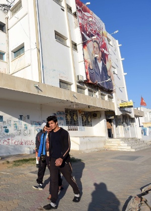 Jovens passam por pôster gigante de Mohamed Bouazizi, o vendedor ambulante cuja imolação deu origem à Primavera Árabe, na cidade de Sidi Bouzid, na Tunísia