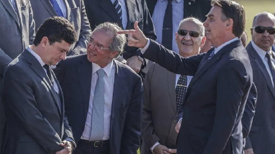 Bolsonaro faz seu gesto tradicional de arminha; o ângulo passa a impressão de que o alvo é Sergio Moro. Eram tempos ainda de amizade tensa. Entre os dois, está Paulo Guedes. Pode ser o próximo - Foto: Gabriela Biló/Estadão