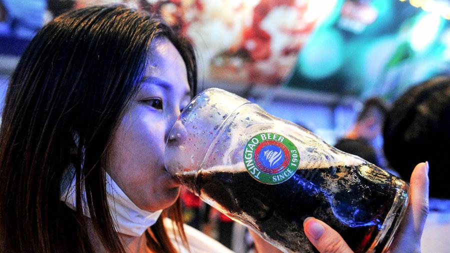Mulher bebe cerveja com máscara no queixo durante o Festival de Qingdao, no leste da China - STR/AFP