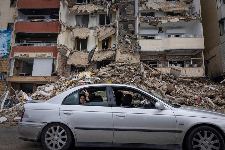 Mulher faz gesto para câmera em frente a prédio destruído após cessar-fogo entre Hezbollah e Israel