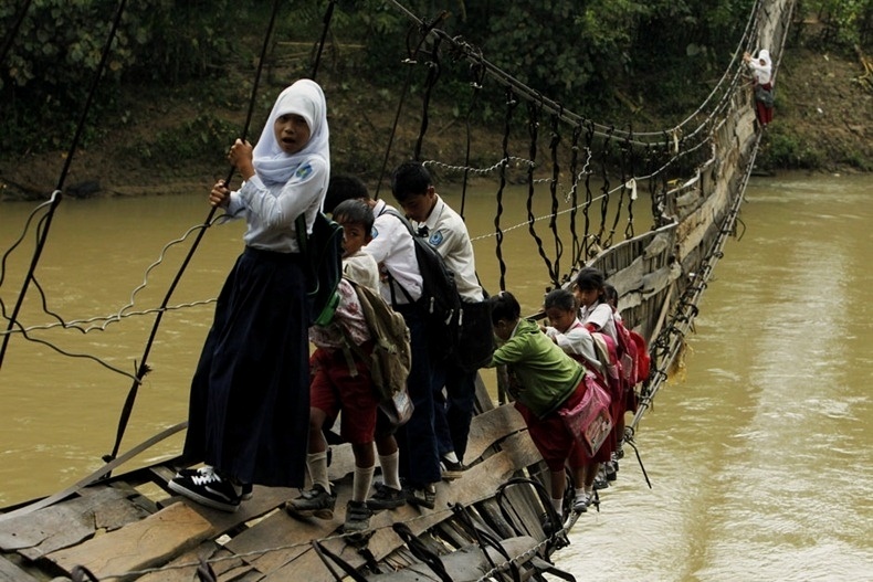 Indonésia - Para ir à escola, crianças atravessam o rio Ciberang por meio de uma ponte quebrada