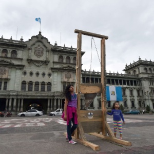 7.set.2015 - Crianças posam para foto ao lado de guilhotina colocada como protesto diante de palácio presencial na Cidade da Guatemala - Rodrigo Arangua/AFP