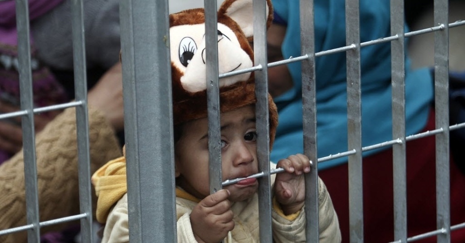 30.dez.2015 - Criança afegã morde a grade de um acampamento improvisado para refugiados em Atenas, na Grécia. Mais de 1 milhão de imigrantes chegaram por meio de rotas marítimas à Europa neste ano, segundo o Alto Comissariado das Nações Unidas para Refugiados. De acordo com o relatório, 844.176 pessoas chegaram na Grécia, usando a rota do Mar Egeu