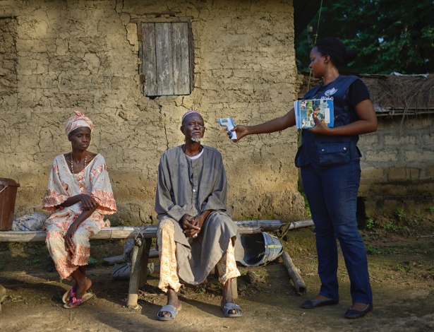 Trabalhadora da OMS mede a temperatura de um homem em Tana, no Guiné - Samuel Aranda/The New York Times