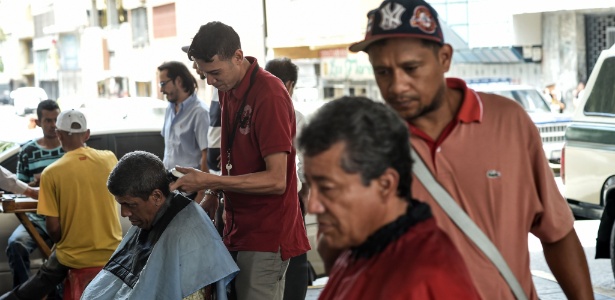 Dois homens trabalham cortando cabelos sob uma ponte em Caracas, Venezuela - Juan Barreto/AFP