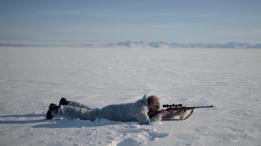 O caçador Hjelmer Hammeken, vestindo um traje camuflado branco, mira uma foca que avistou a 300 metros de distância