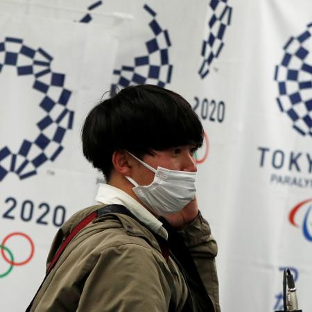 Homem com máscara de proteção em frente à logomarca dos Jogos Tóquio 2020 - ISSEI KATO