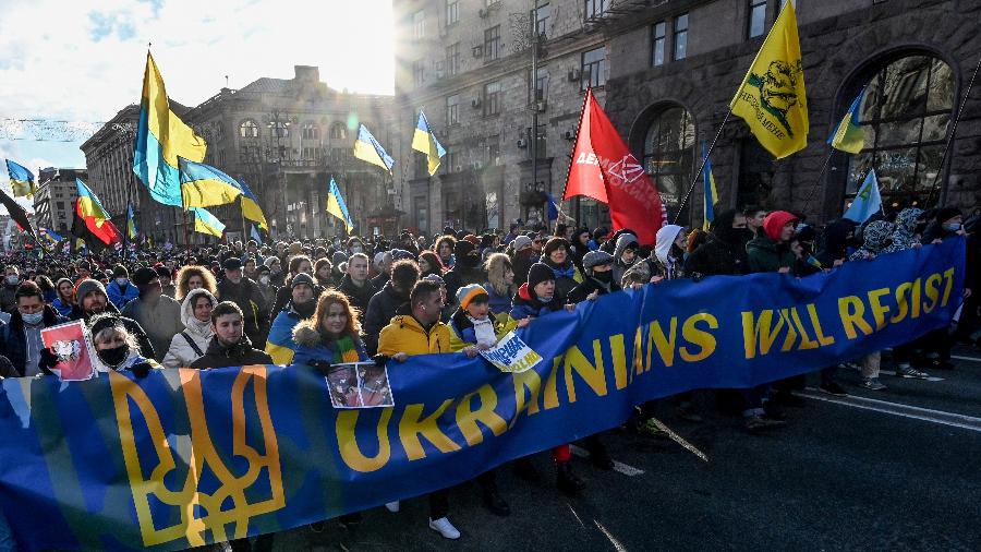 12.fev.2022 -  Manifestantes gritam slogans enquanto marcham atrás de uma faixa que diz "Os ucranianos resistirão" nas cores da bandeira nacional durante um comício em Kiev - Sergei Supinsky/AFP