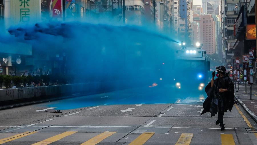Manifestante corre à frente de um caminhão com canhão de água e tinta azul disparado pelas forças de segurança de Hong Kong - Dale de la Rey/AFP