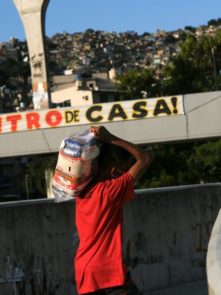 Um menino carrega doações entregues na favela da Rocinha durante a pandemia no Rio de Janeiro - RICARDO MORAES/REUTERS