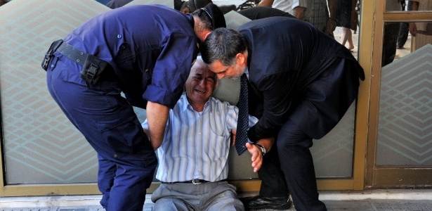 Um aposentado chora e é amparado por um gerente e um policial em agência bancária de Salônica, na Grécia - Sakis Mitrolidis - 3.jul.2015/AFP