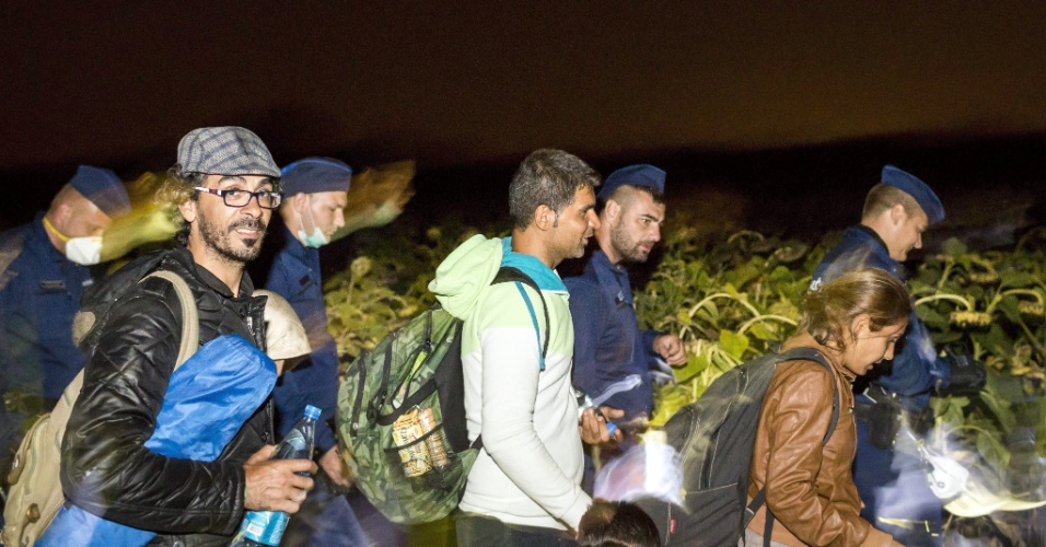 13.set.2015 - Policiais húngaros escoltam imigrantes que atravessaram a fronteira do país com a Sérvia no fim da noite de sábado (12). A cena foi registrada em Roszke, cerca de 180 quilômetros a sudeste da capital, Budapeste. Na última sexta (11), o primeiro-ministro da Hungria, Viktor Orban, alertou que quem atravessasse a fronteira do país com o território sérvio seria "preso imediatamente"
