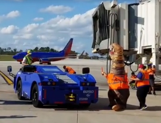 Um funcionário da companhia aérea se fantasiou de dinossauro para orientar um avião no aeroporto - Reprodução/Facebook Orlando International Airport (MCO)