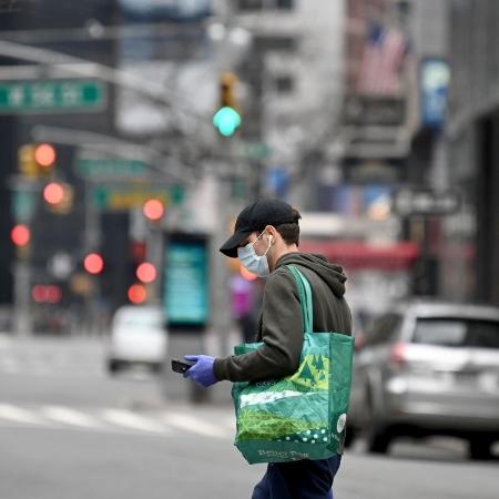 Homem usa luvas e máscara de proteção ao carregar sua sacola de compras em Nova York - Alexi Rosenfeld/Getty Images