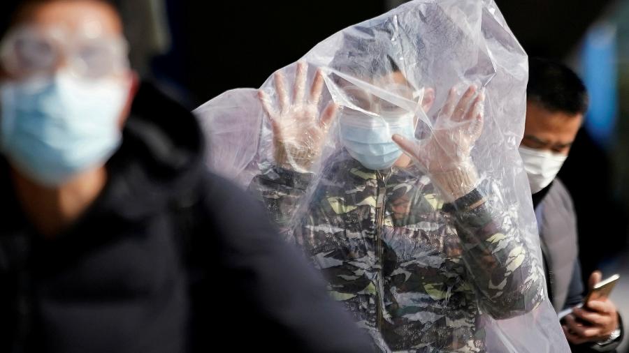 Homem caminha na estação de trem de Xangai, na China, coberto com uma sacola plástica em meio ao aumento de casos de coronavírus no país - ALY SONG/REUTERS