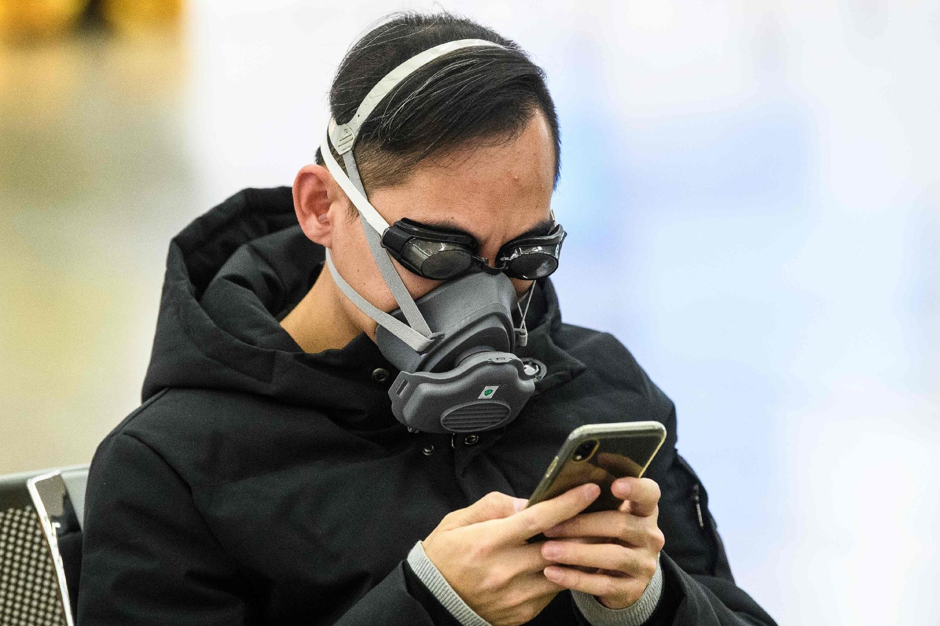 28.jan.2020 - Um passageiro usa óculos de natação e máscara facial enquanto espera o trem dentro da estação que liga Hong Kong à China - ANTHONY WALLACE/AFP