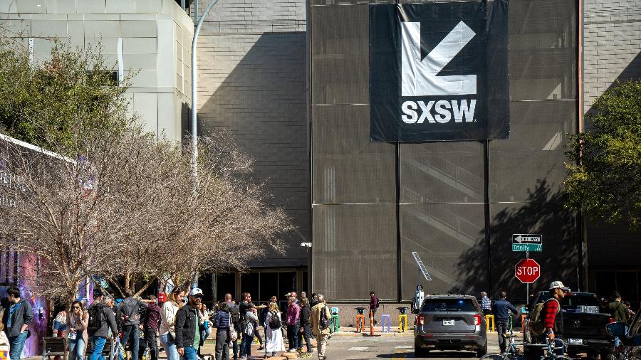 Pessoas caminhando em frente a um banner do SXSW (South by Southwest), maior festival de inovação e criatividade do mundo