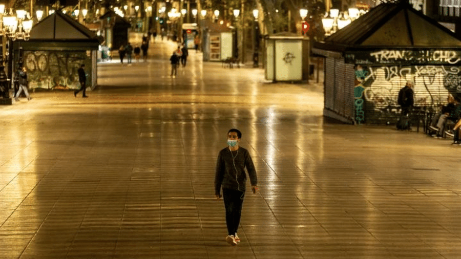 Homem de máscara caminha em rua de pedestres à noite - EPA/ENRIC FONTCUBERTA