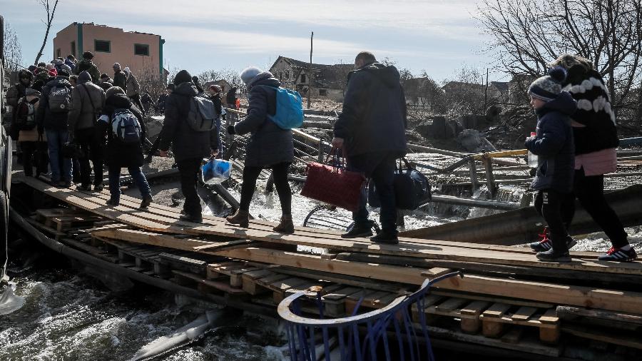 Pessoas atravessam rio em ponte destruída enquanto evacuam da cidade de Irpin, em meio à invasão russa da Ucrânia - REUTERS/Gleb Garanich