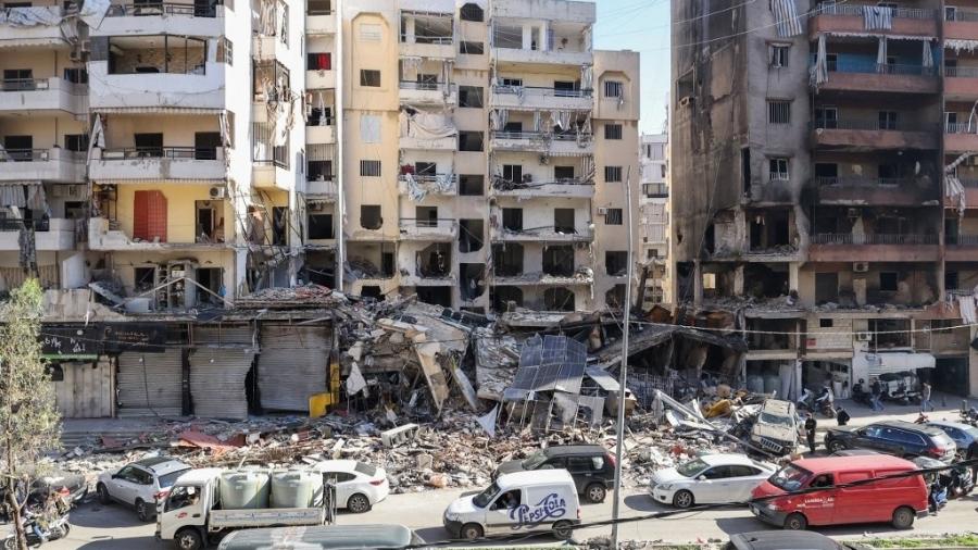 Carros passam por edifícios que foram danificados ou destruídos em ataques israelenses no bairro Hay el-Sellom, subúrbio ao sul de Beirute