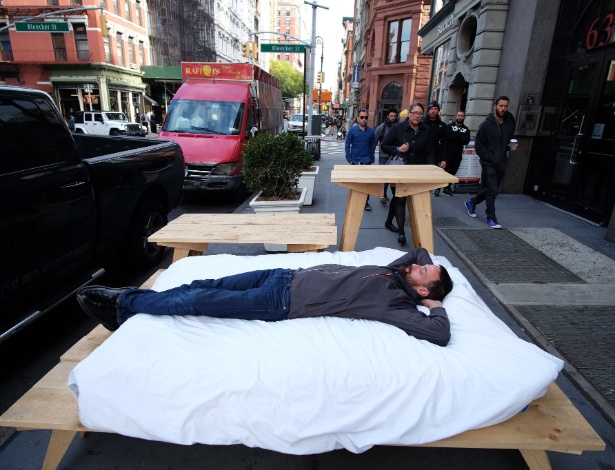 O artista francês Sebastien Renauld deita em cama colocada em uma calçada da Broadway, em Nova York (EUA) - Jewel Samad/AFP