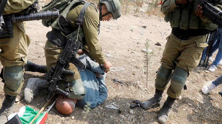Soldado israelense ajoelhado no pescoço de um militante palestino - RANEEN SAWAFTA/REUTERS