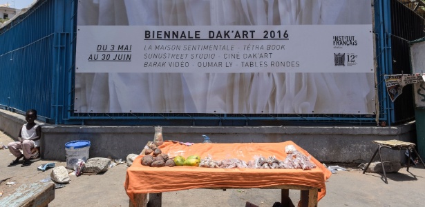 Barraca de frutas é vista diante de cartaz da Bienal de Dacar, em Dacar, no Senegal - Seyllou/AFP