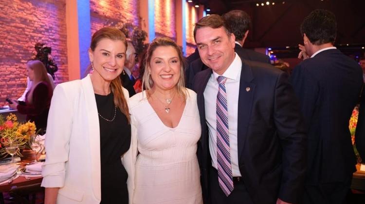 Daniella Marques entre o casal Flávio Bolsonaro e Fernanda durante evento da Caixa, em 2022