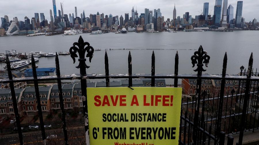 Cartaz promovendo distanciamento social está pendurado em uma cerca no Hamilton Park, acima do rio Hudson, com o horizonte da cidade de Nova York - MIKE SEGAR/REUTERS