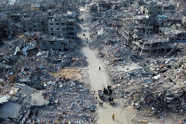 Foto aérea mostra pessoas atravessando estrada entre escombros em Rafah, no sul da Faixa de Gaza, nesta segunda-feira (20)