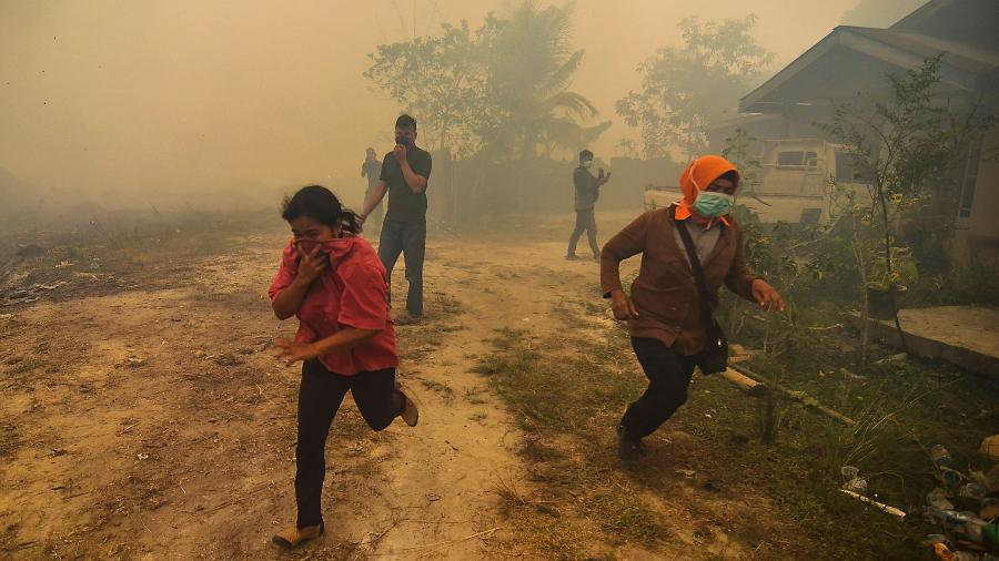22.set.2019 - Moradores de um vilarejo fogem com a chegada de um incêndio florestal em Kampar, Riau, na Indonésia - Wahyudi/AFP
