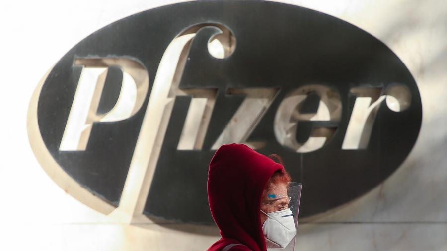 Mulher veste um protetor facial enquanto passa pela frente da sede da Pfizer em Nova York - Kena Betancur/AFP