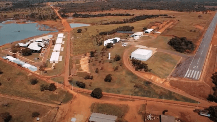 Vista aérea da fazenda. À esquerda, as estruturas para o cuidado com os gados. No centro, as casas da família. À direita, a pista para pousos e decolagens Vista aérea da fazenda. À esquerda, as estruturas para o cuidado com os gados. No centro, as casas da família. À direita, a pista para pousos e decolagens