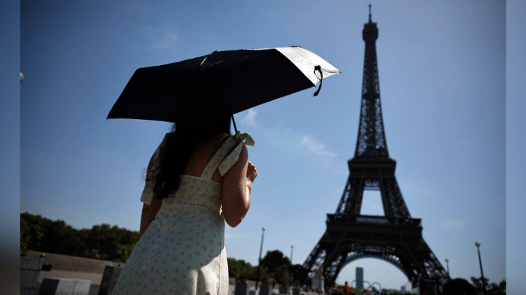 Mulher se protege do sol sob um guarda-chuva enquanto caminha em direção à Torre Eiffel, em Paris, na França, enquanto uma onda de calor recorde atinge parte da Europa